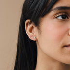 Close-up of a woman wearing Pave Round Studs, small round earrings adorned with sparkling pave gems, highlighting her ear and part of her face.