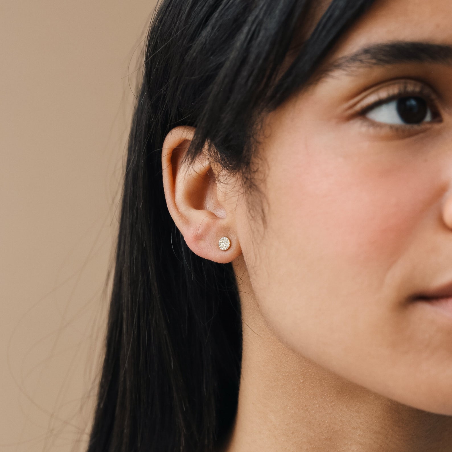 Close-up of a woman wearing Pave Round Studs, small round earrings adorned with sparkling pave gems, highlighting her ear and part of her face.
