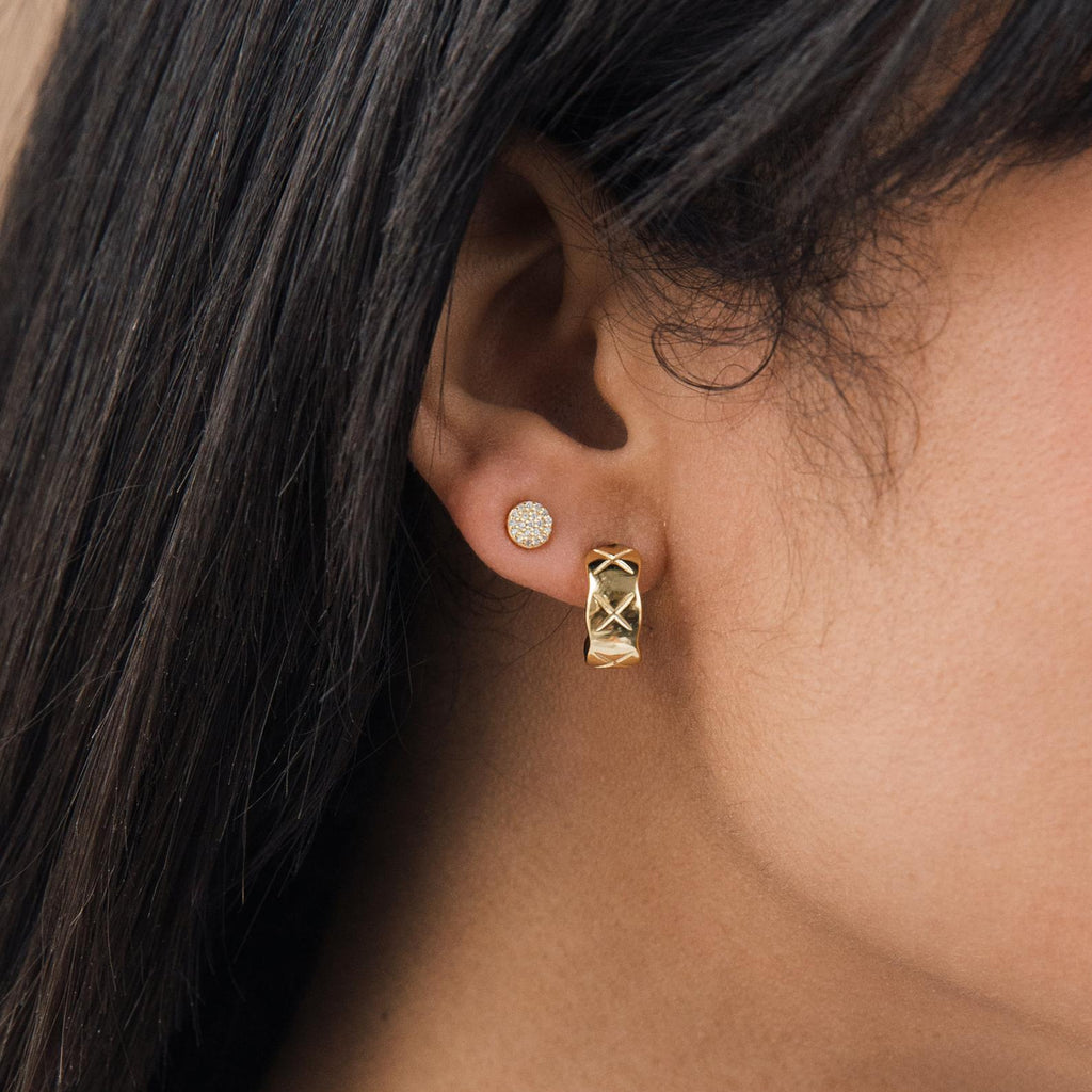 Close-up of a woman's ear wearing two gold earrings: Pave Round Studs and a textured hoop—perfect for layering in your glam jewelry collection.