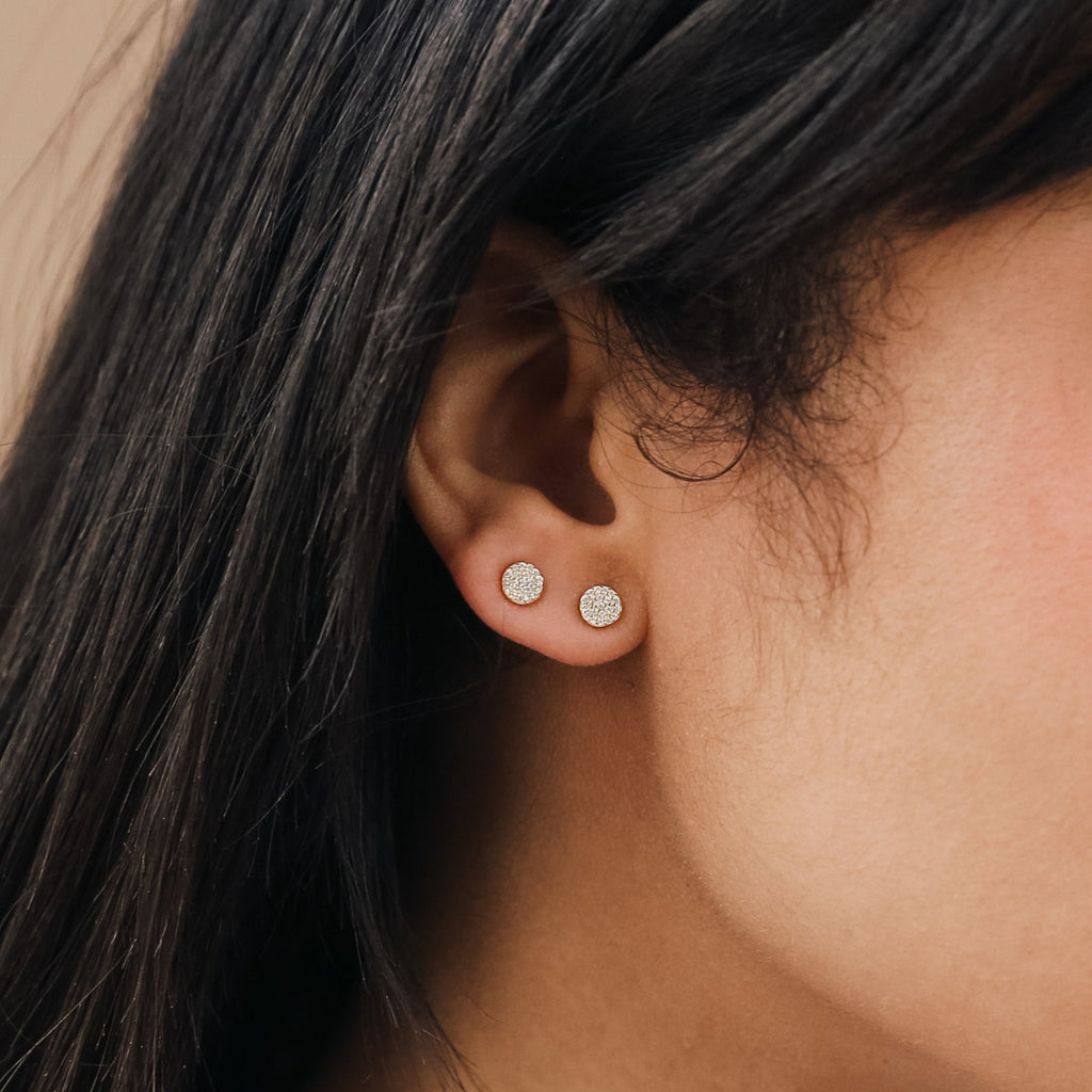 Close-up of a woman's ear wearing two pairs of Pave Round Studs—small, round, sparkling gem stud earrings—in each lobe.