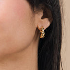 Close-up of a woman's ear wearing Diana Hoops—chunky, twisted croissant-style earrings that make a bold statement.
