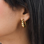 Close-up of a woman's ear with dark straight hair wearing the chunky gold Diana Hoops earring.