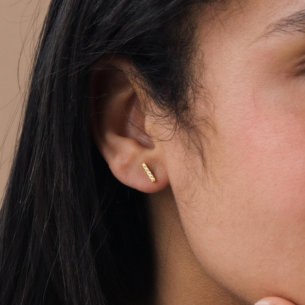 Close-up of a person’s ear wearing small, gold Pave Bar Studs—ideal for those who love minimal jewelry.