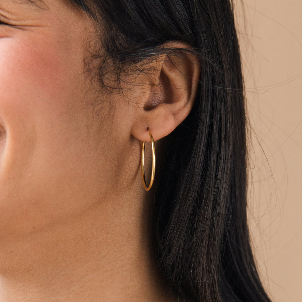 Close-up of a woman's ear wearing the Large Thin Hoops, featuring a delicate gold design that adds subtle elegance to any everyday outfit, shown against a neutral background.