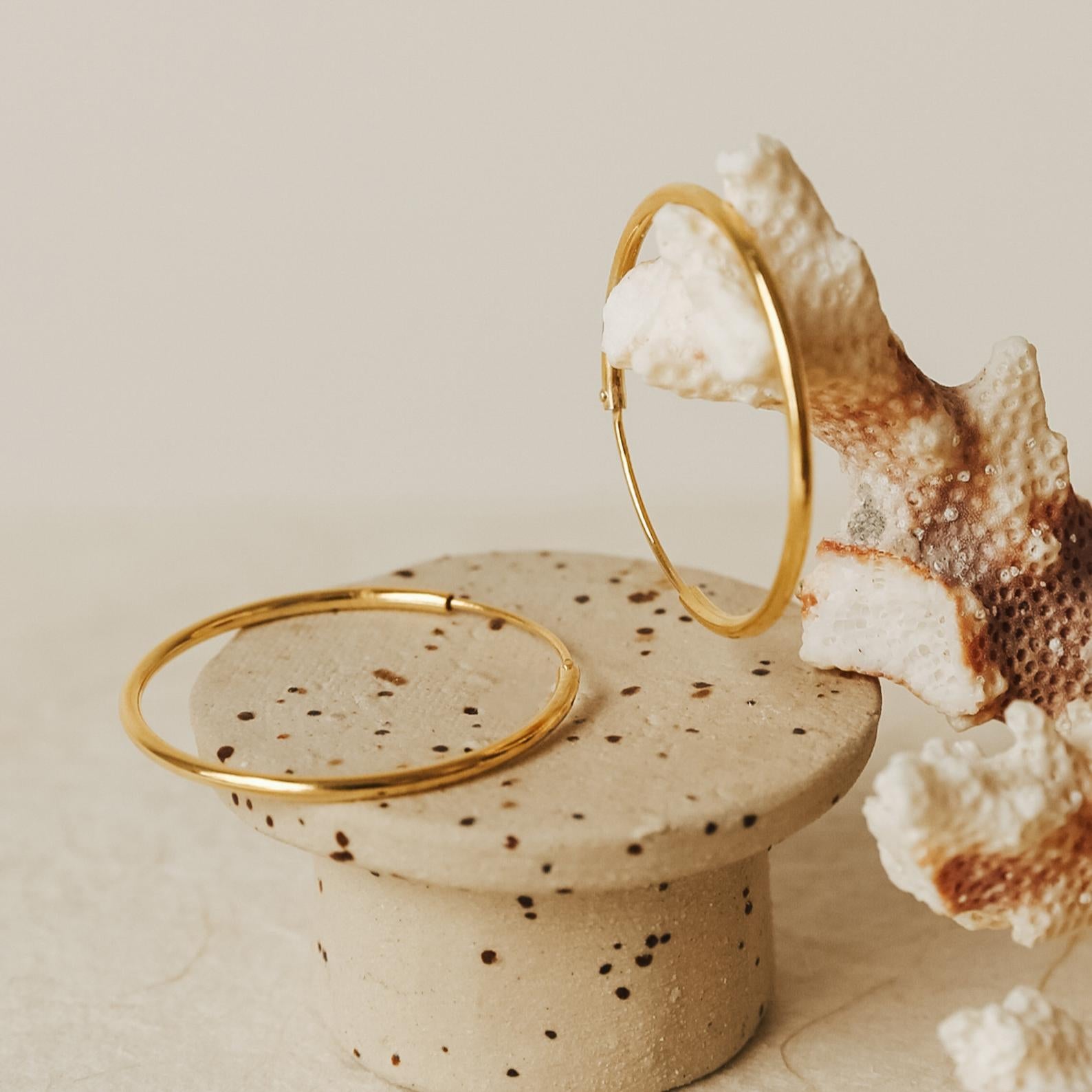 Endless Thin Hoops—elegant gold earrings showcased on a speckled stone stand with coral. Designed as an everyday accessory for timeless style.