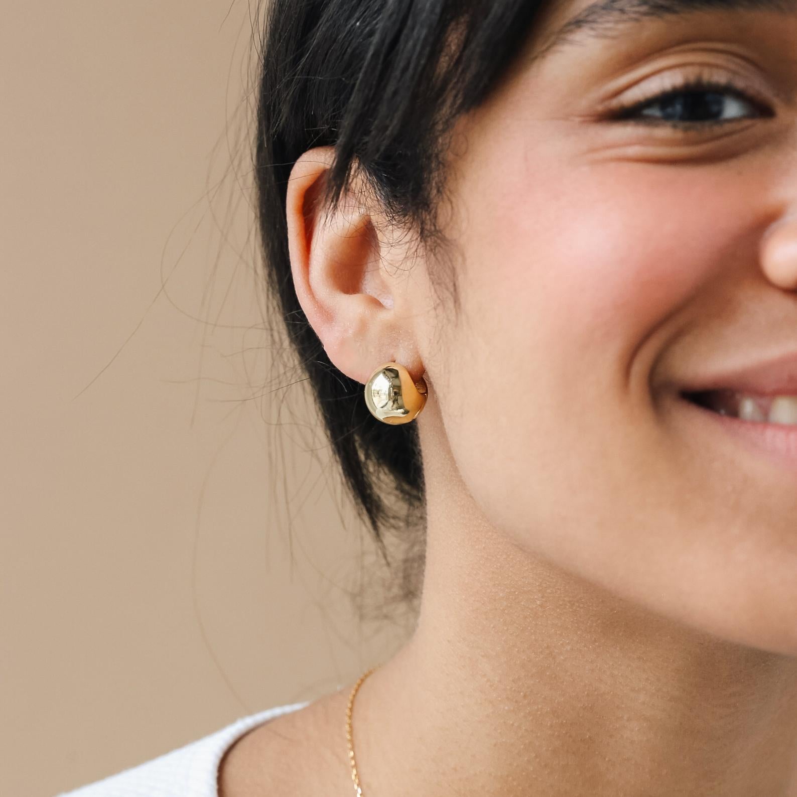 Close-up of a woman smiling, wearing gold stud earrings, a delicate gold necklace, and our Chunky Ball Hoops—bold, 70’s-inspired earrings for a timeless look.