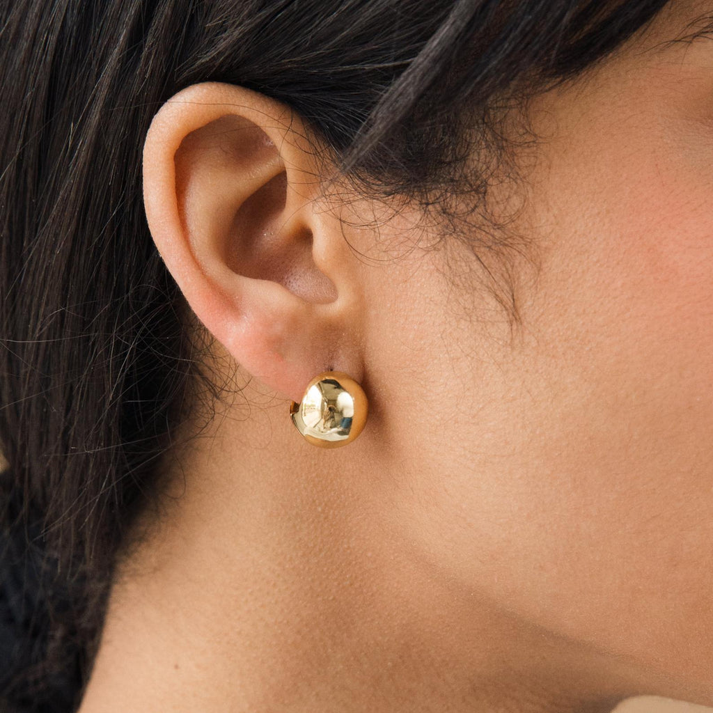 Close-up of a person wearing Chunky Ball Hoops, shiny round gold earrings that radiate a subtle 70’s-inspired vibe reminiscent of classic chunky styles.