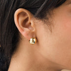 Close-up of a person wearing Chunky Ball Hoops, shiny round gold earrings that radiate a subtle 70’s-inspired vibe reminiscent of classic chunky styles.