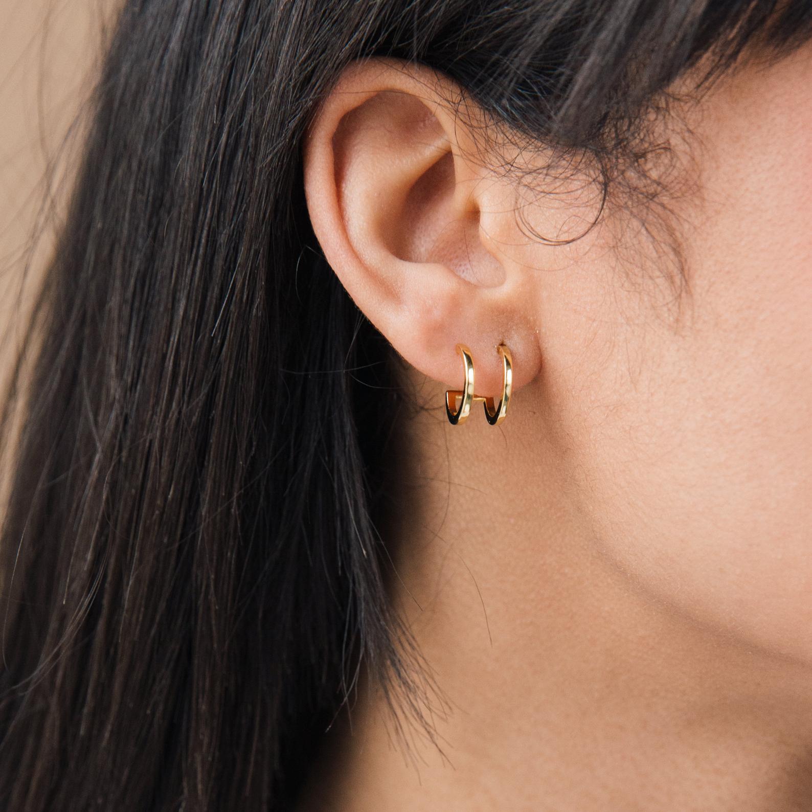 Close-up of a woman's ear adorned with Twin Hoops, creating a double earring illusion, paired with straight dark hair.