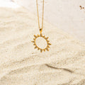 Gold sun-shaped pendant necklace resting on sand, featuring a hollow center and spiked edges embellished with pave set stones.