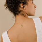 A woman with curly hair wears the Crescent Moon Necklace backwards, showcasing its elegant amulet on her bare back while dressed in white.