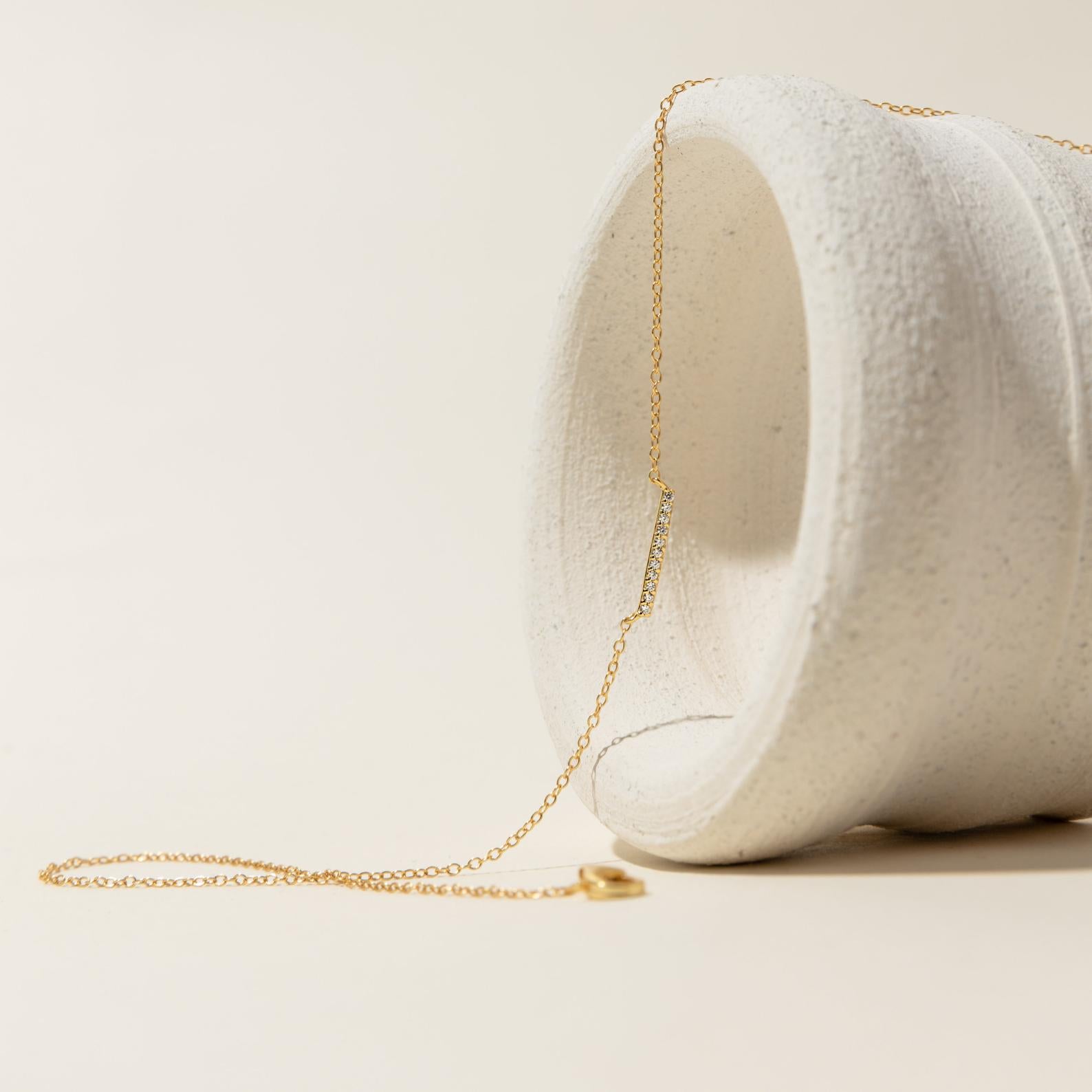 The Pave Bar Necklace is elegantly draped over a textured white ceramic vase, displayed against a neutral background.