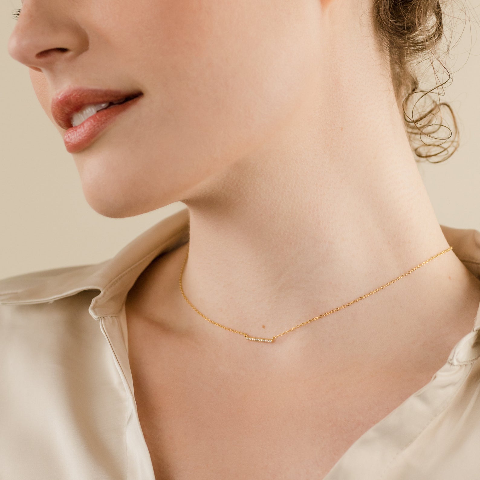 A woman wears the Pave Bar Necklace layered with other chic necklaces over a cream silk blouse, shown from the shoulders up.