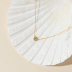 The Pave Round Necklace with a silver chain is displayed on a white seashell against a beige background.