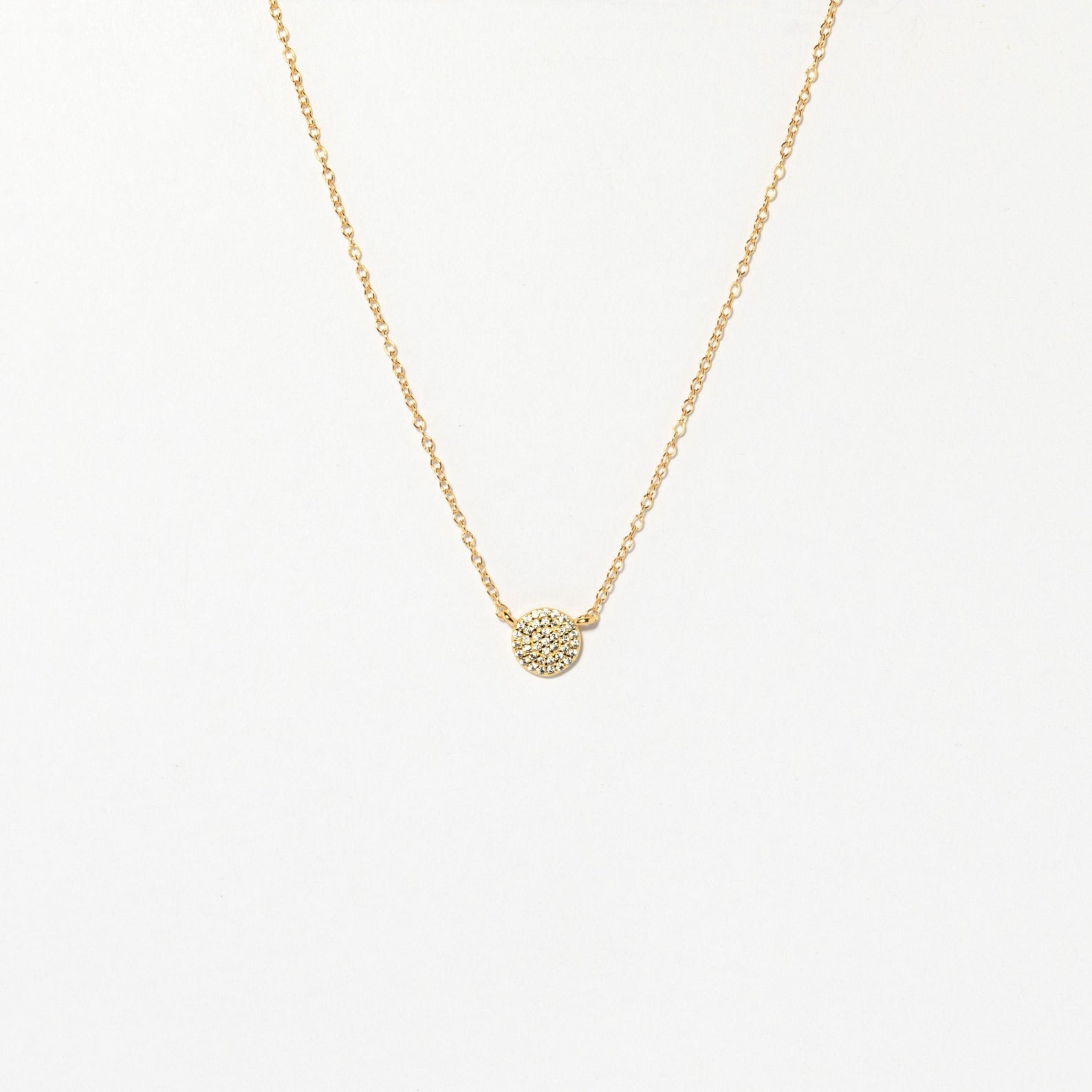 The Pave Round Necklace features a gold chain with a small, pavé-encrusted circle pendant, shown on a plain white background.
