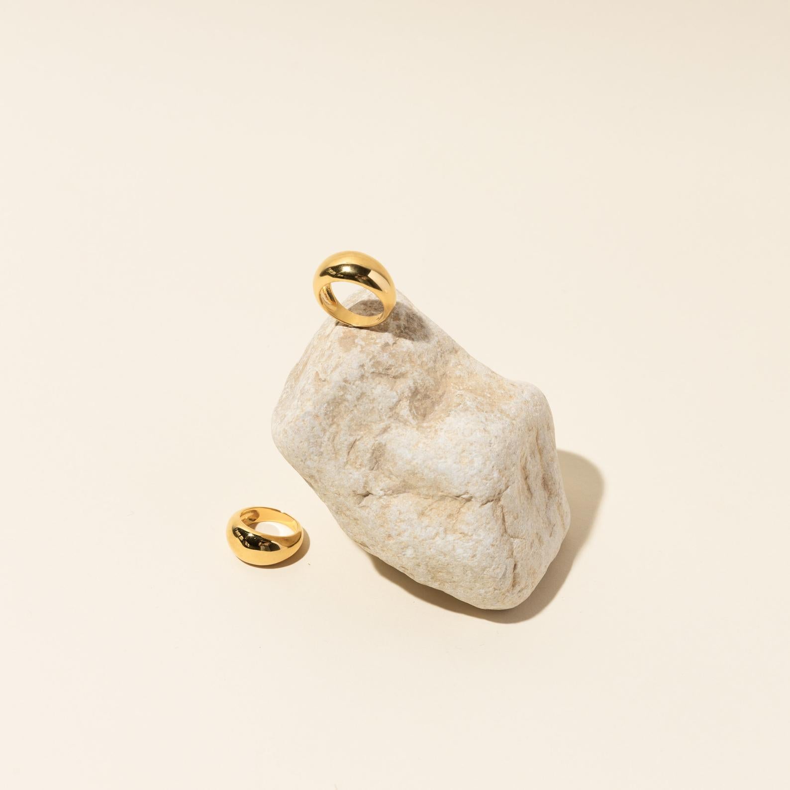 The Bold Dome Ring, showcased on a light stone with another beside it, shines against a beige background.
