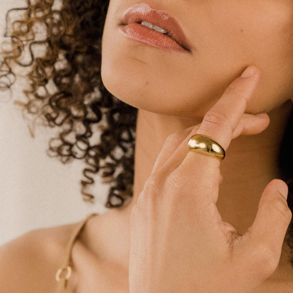 A woman with curly hair touches her face, showing off the Bold Dome Ring and nude lipstick.