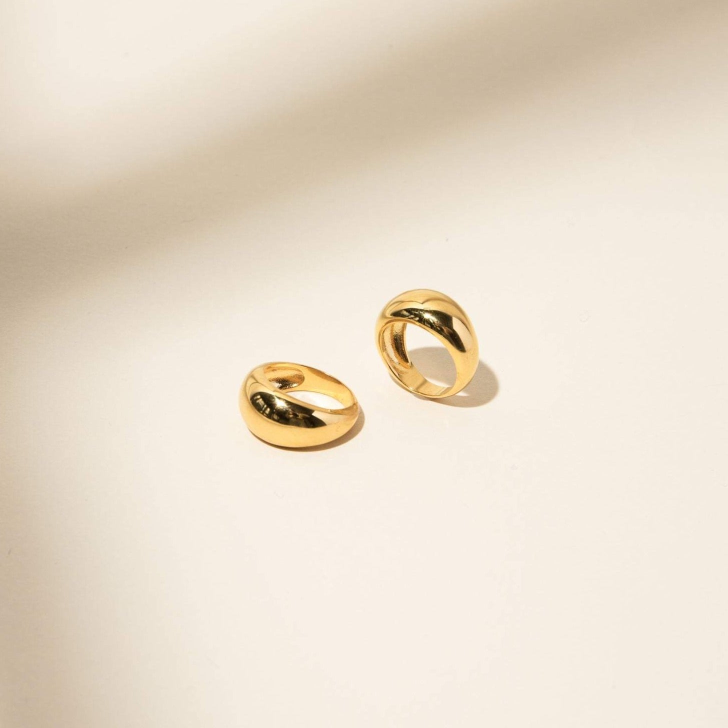 Two gold, chunky hoop earrings rest on a light beige surface with soft shadows—perfect to pair with your favorite Bold Dome Ring or stacking rings for a statement look.