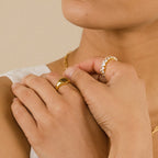 A person wearing elegant jewelry, including the Alannah Ring and a gold necklace, holds their hands near their face.