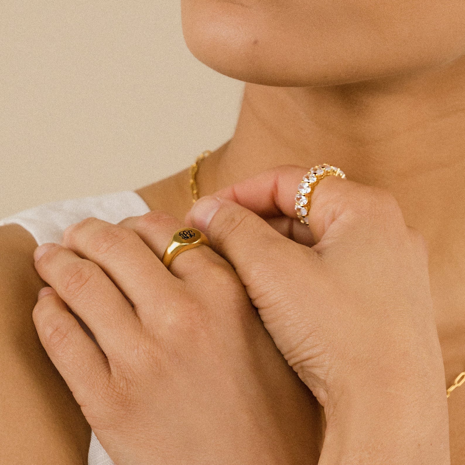 A person wearing elegant jewelry, including the Alannah Ring and a gold necklace, holds their hands near their face.