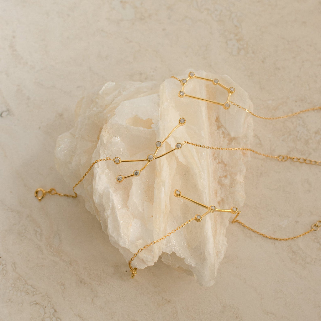 The Constellation Bracelet features a minimal gold design with small crystals, displayed on a white stone background—a unique jewelry piece that brings subtle elegance to any look.