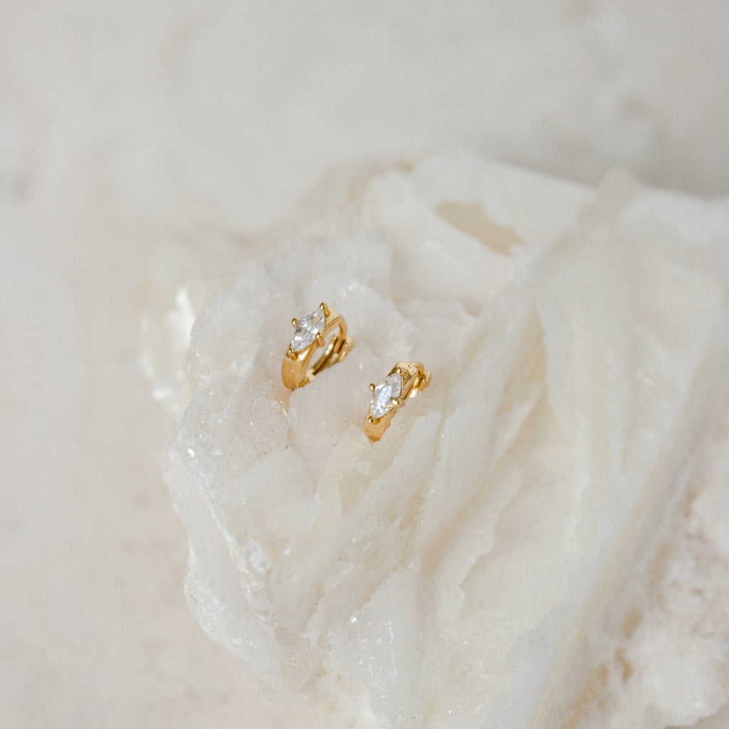 Aurora Huggies: Dainty gold hoops featuring sparkling diamond accents, shown resting on a textured white crystal.