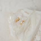 Aurora Huggies: Dainty gold hoops featuring sparkling diamond accents, shown resting on a textured white crystal.