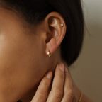 Close-up of a woman's ear wearing Willow Huggies—small gold hoop earrings crafted in 925 sterling silver—as she gently touches her neck.