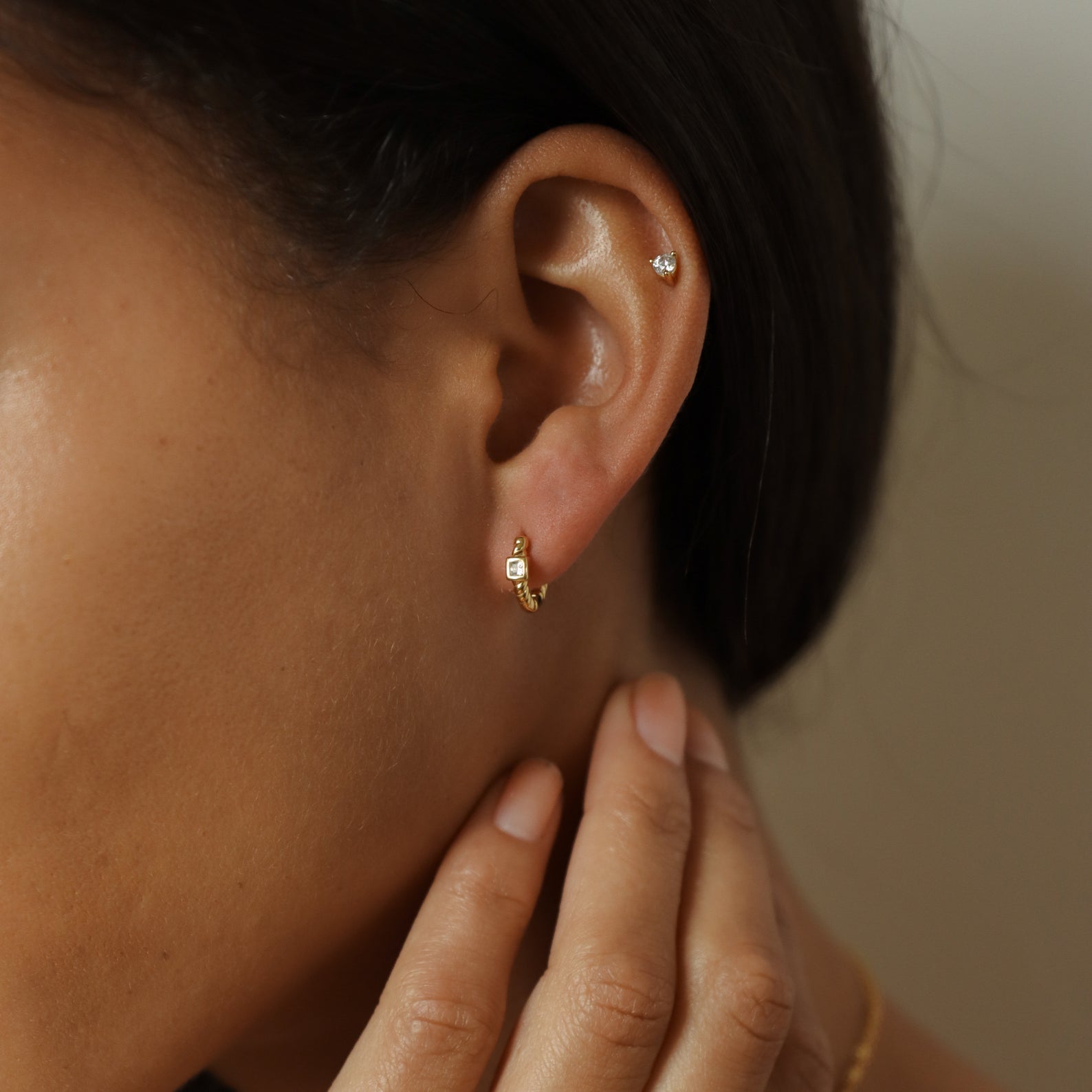 Close-up of a woman's ear wearing Willow Huggies—small gold hoop earrings crafted in 925 sterling silver—as she gently touches her neck.