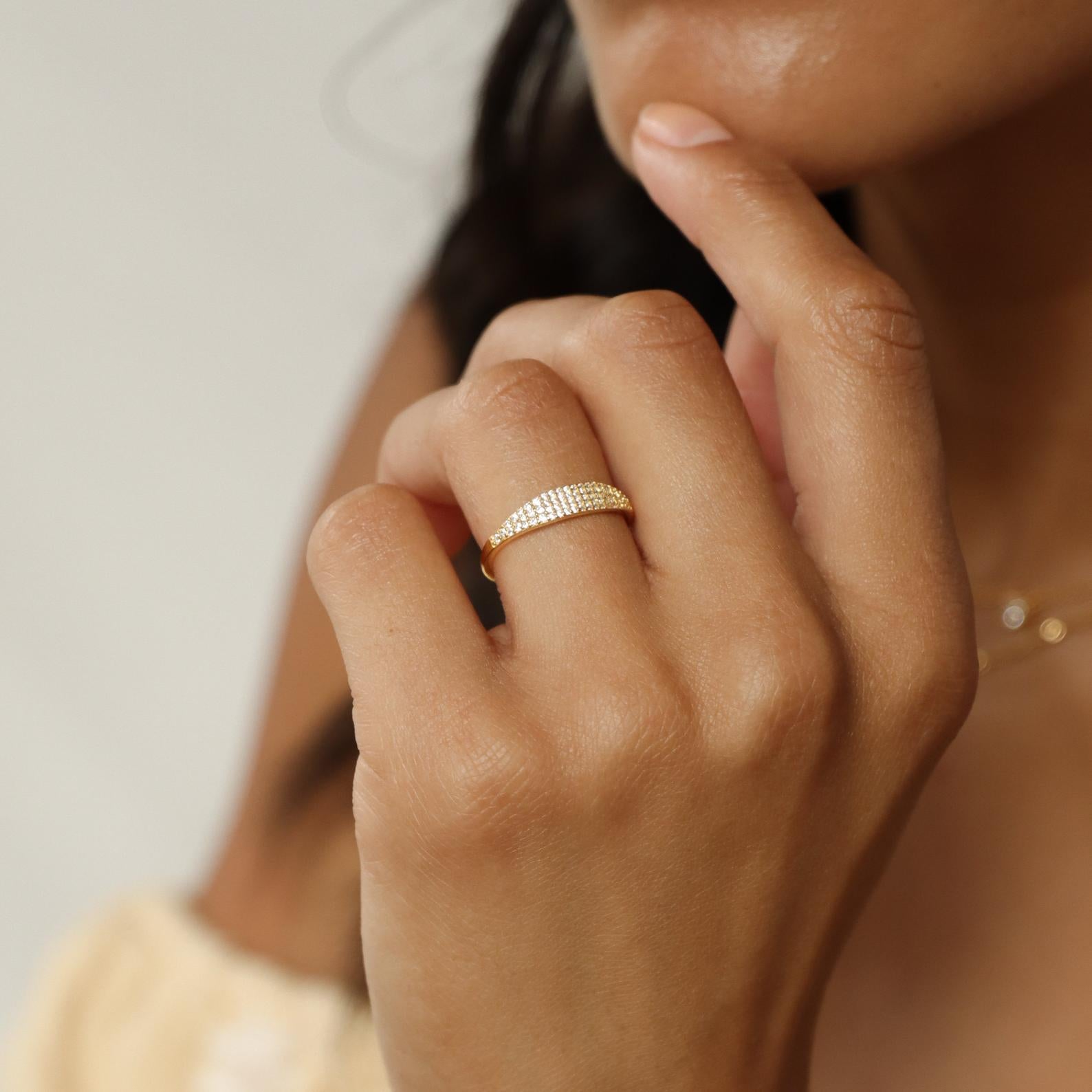 A person wearing the Gina Pave Signet Ring in gold with small diamonds rests their hand near their chin.