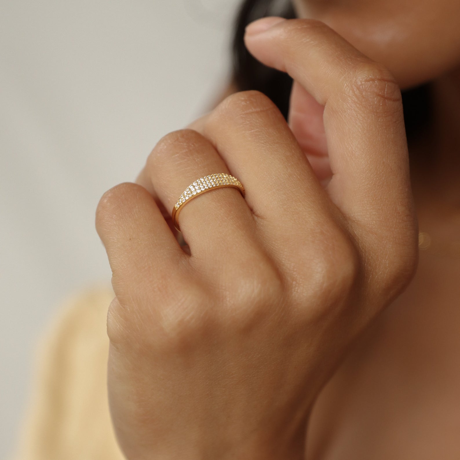 A hand adorned with the Gina Pave Signet Ring, its gold band set with pavé diamonds sparkling as fingers softly rest on the chin.