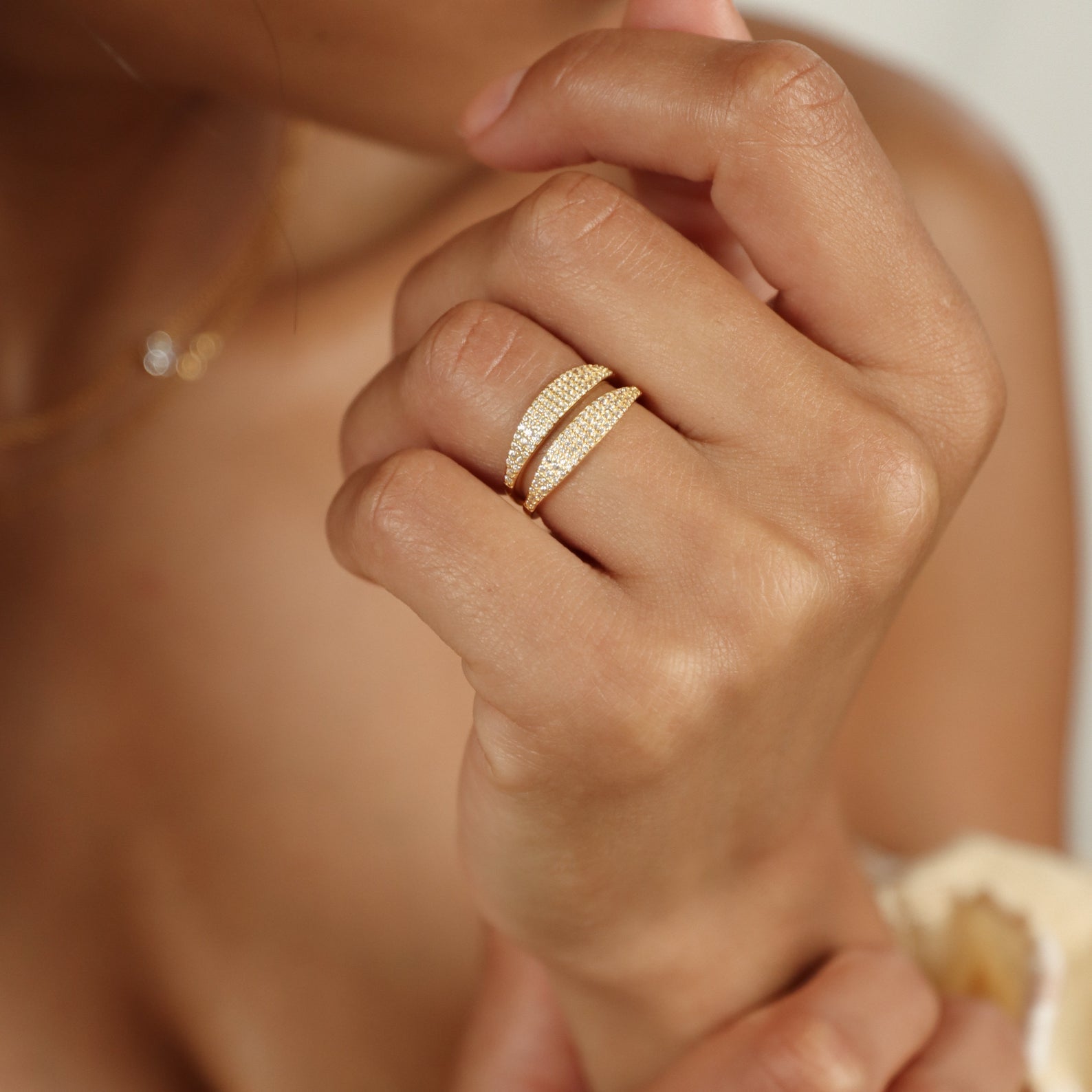 A hand wearing the Gina Pave Signet Ring, a gold double-band ring with sparkling stones, held near the face.
