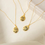 Three gold Oval Pet Necklaces engraved with cat faces and names—Bella, Luna, and Sammy—rest on a soft cream fabric. The Oval Pet Necklace is a meaningful way to celebrate your furry friends with personalized jewelry.