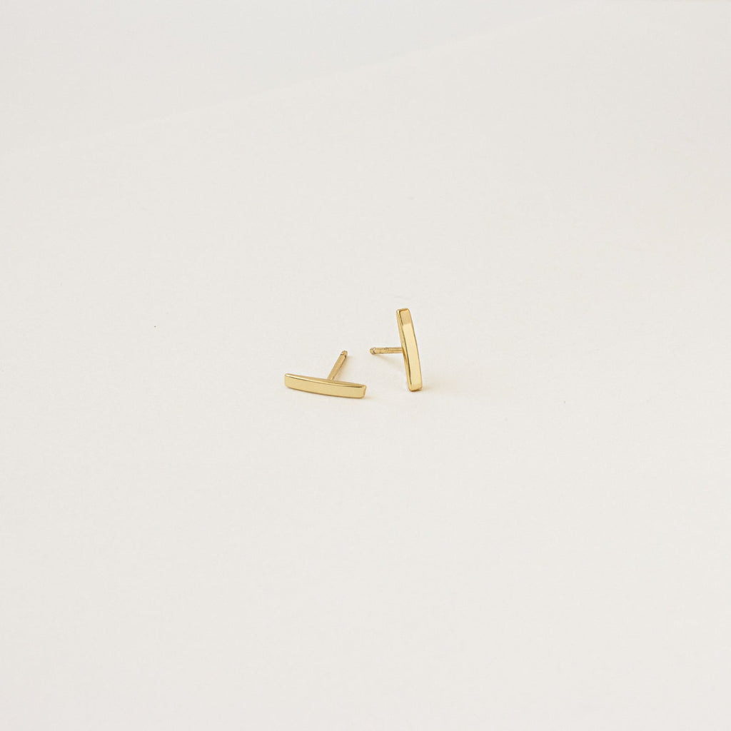 The Dainty Bar Studs in gold are perfect for a minimalist earrings look or layering in your earring stack, shown on a plain white background.