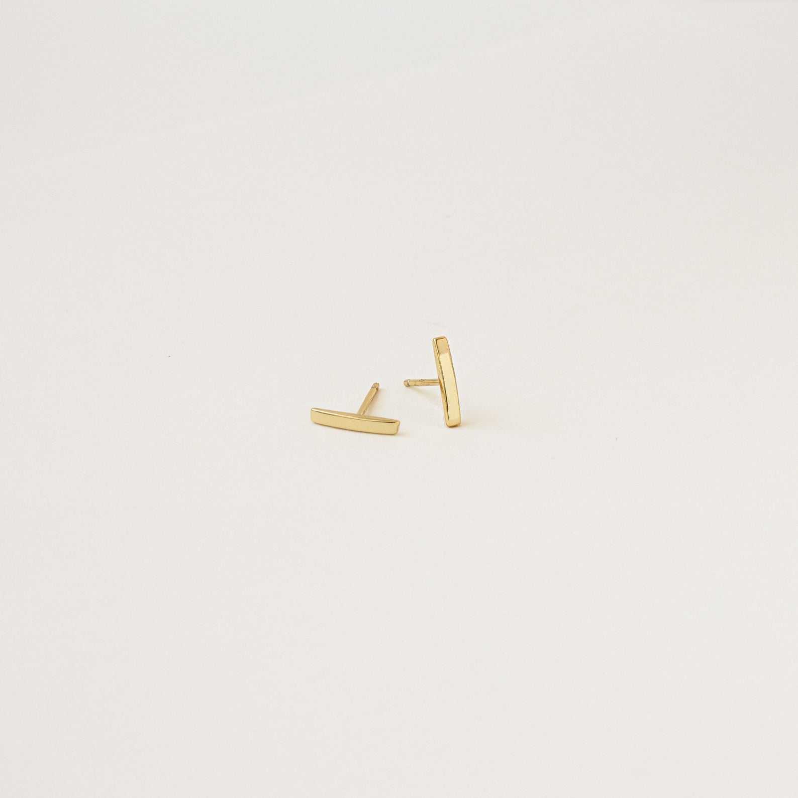 The Dainty Bar Studs in gold are perfect for a minimalist earrings look or layering in your earring stack, shown on a plain white background.