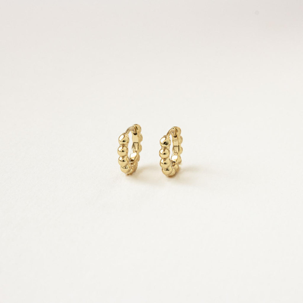 The Dainty Sphere Beaded Huggies are minimalistic gold hoop earrings with a delicate beaded design, displayed against a plain white background.