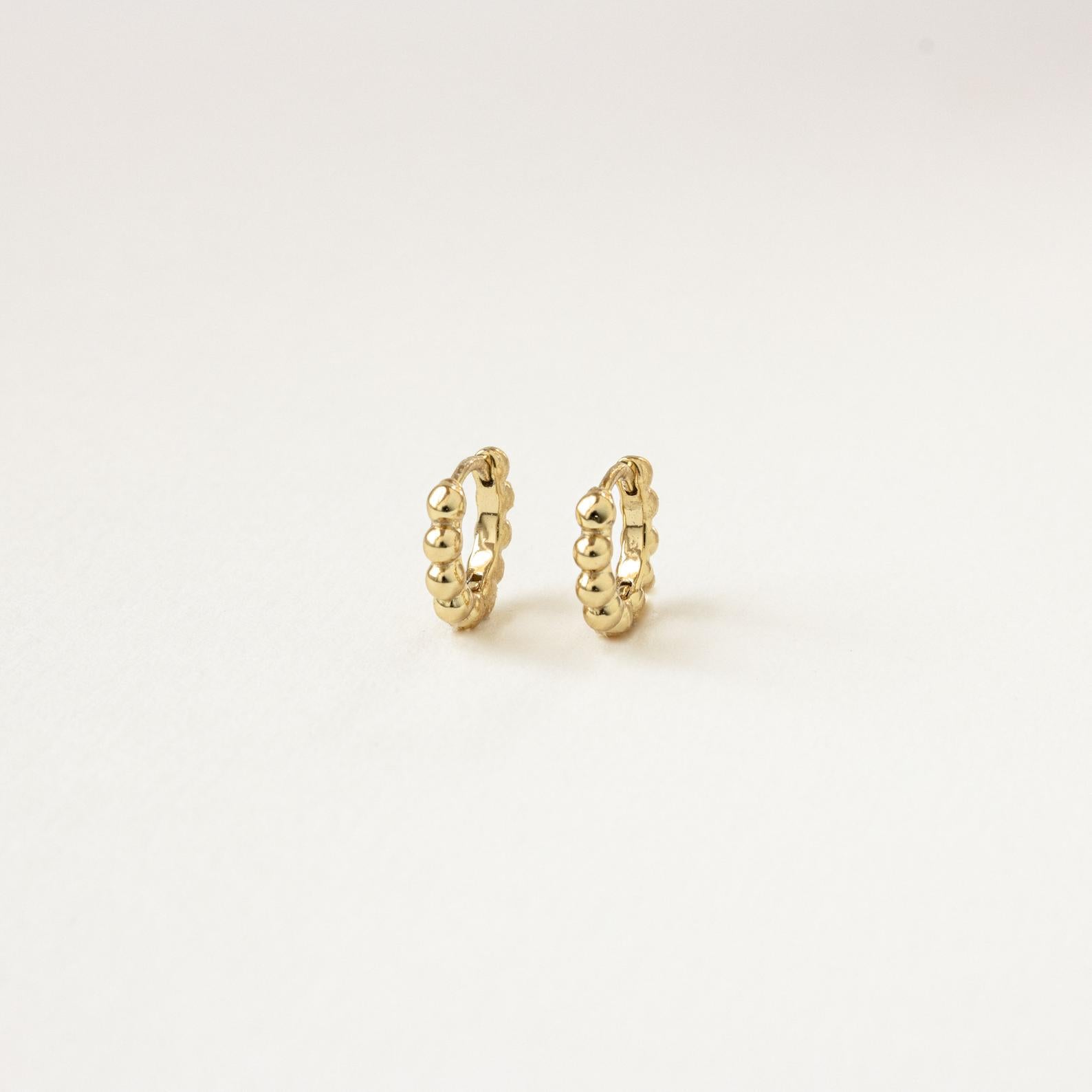 The Dainty Sphere Beaded Huggies are minimalistic gold hoop earrings with a delicate beaded design, displayed against a plain white background.