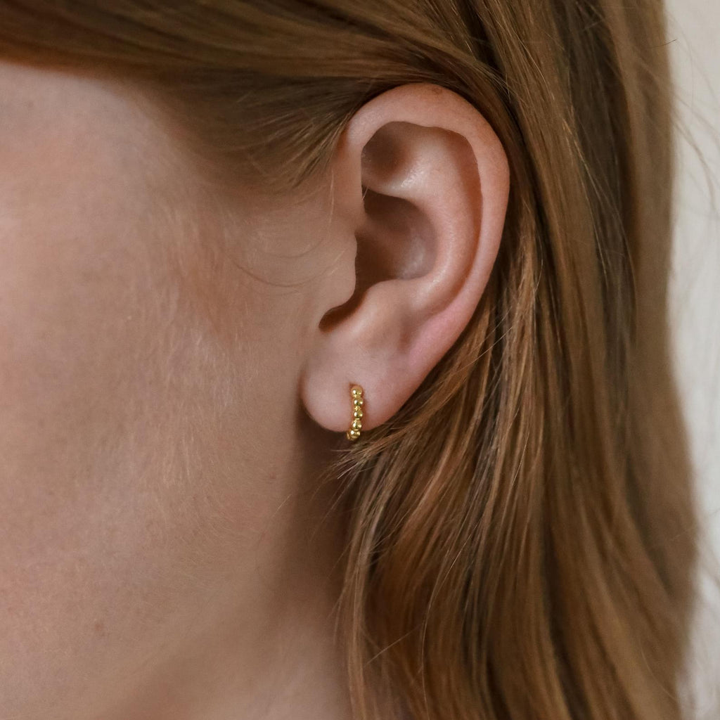 Close-up of a woman's ear wearing Dainty Sphere Beaded Huggies, highlighting the elegant and minimalistic gold hoop earrings.