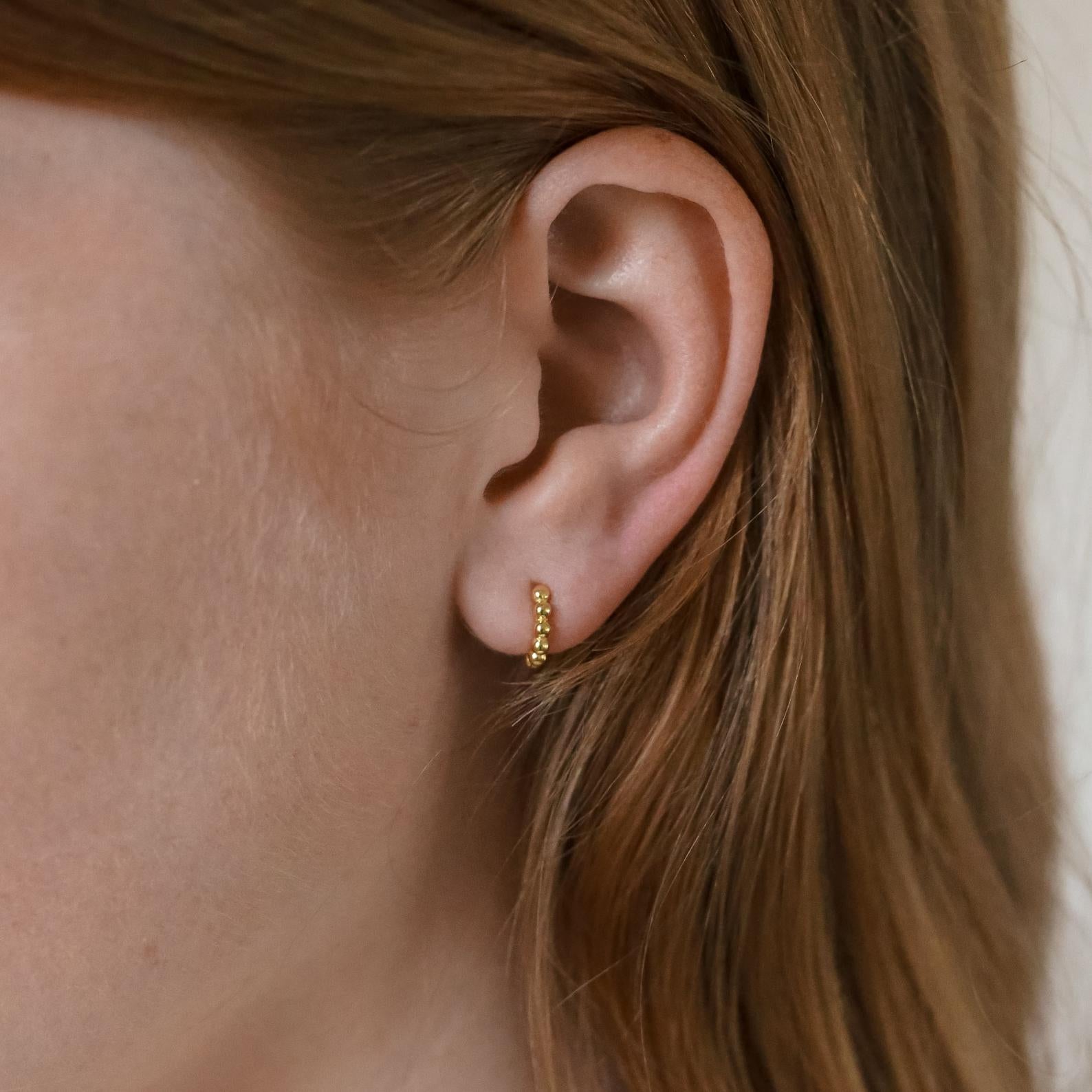 Close-up of a woman's ear wearing Dainty Sphere Beaded Huggies, highlighting the elegant and minimalistic gold hoop earrings.