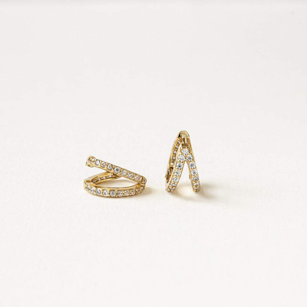 The Esther Duo Pave Huggies are gold double hoop earrings with sparkling gemstones, shown on a plain white background.