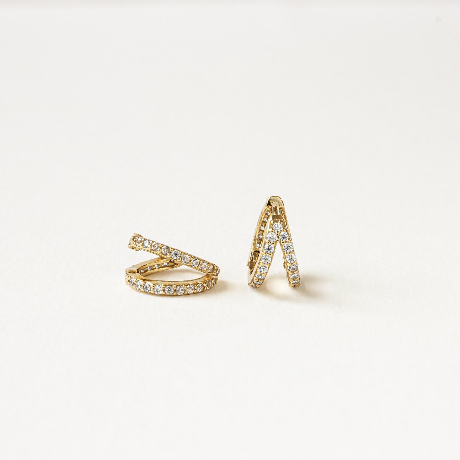 The Esther Duo Pave Huggies are gold double hoop earrings with sparkling gemstones, shown on a plain white background.