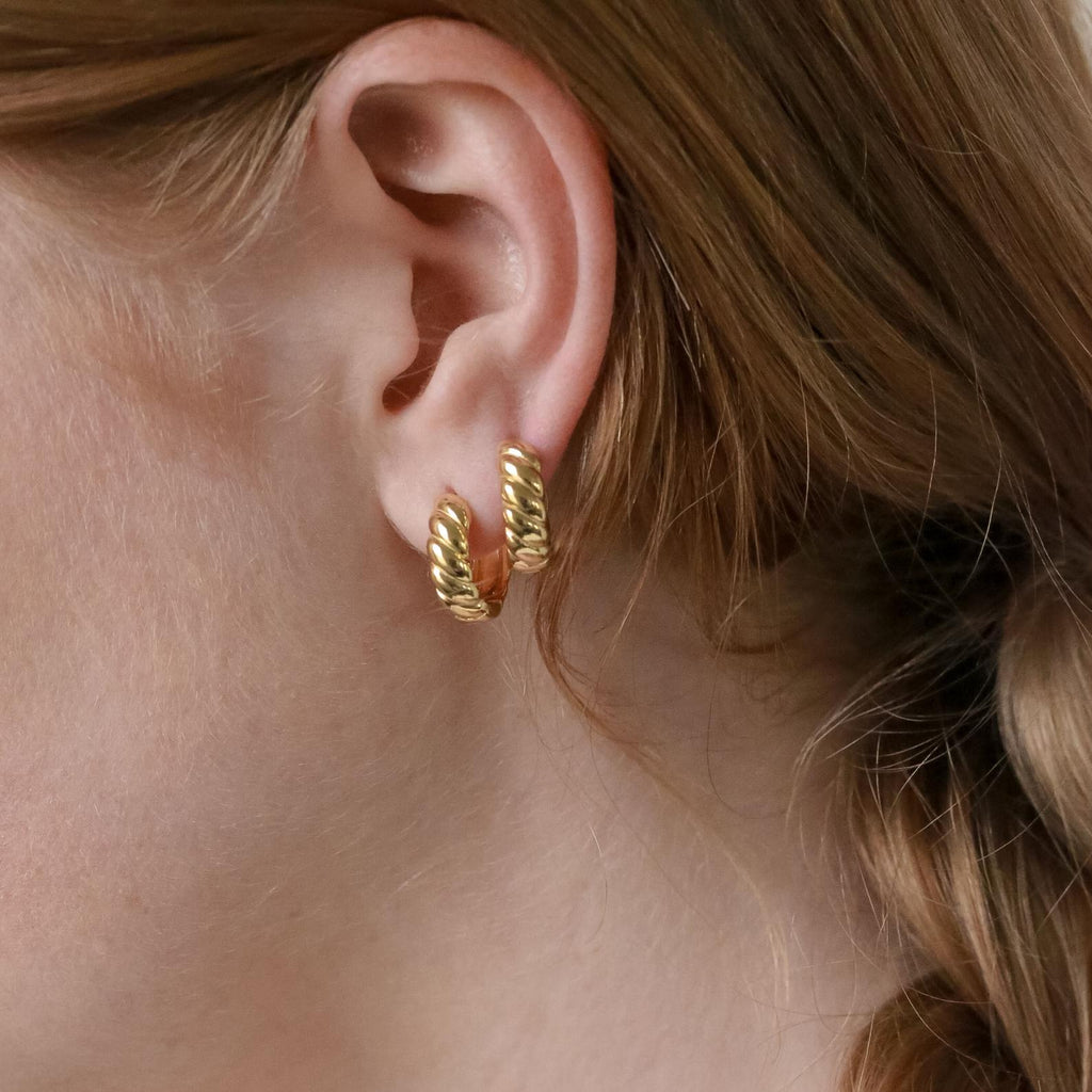 Close-up of a woman's ear wearing two Morgan Croissant Hoops, chunky gold twisted earrings that capture the effortless French girl aesthetic with these modern accessories.
