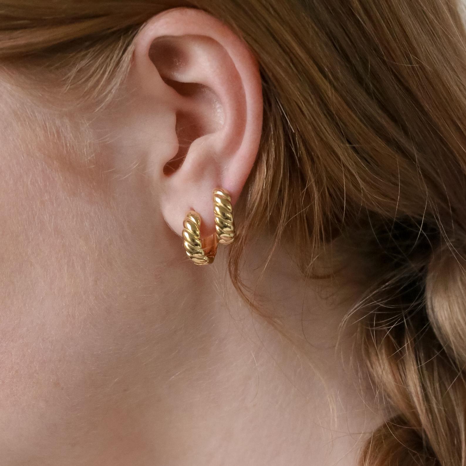 Close-up of a woman's ear wearing two Morgan Croissant Hoops, chunky gold twisted earrings that capture the effortless French girl aesthetic with these modern accessories.
