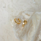 Audrey Huggies displayed on a textured, crystalline white stone surface—an ideal everyday accessory that effortlessly elevates any look.