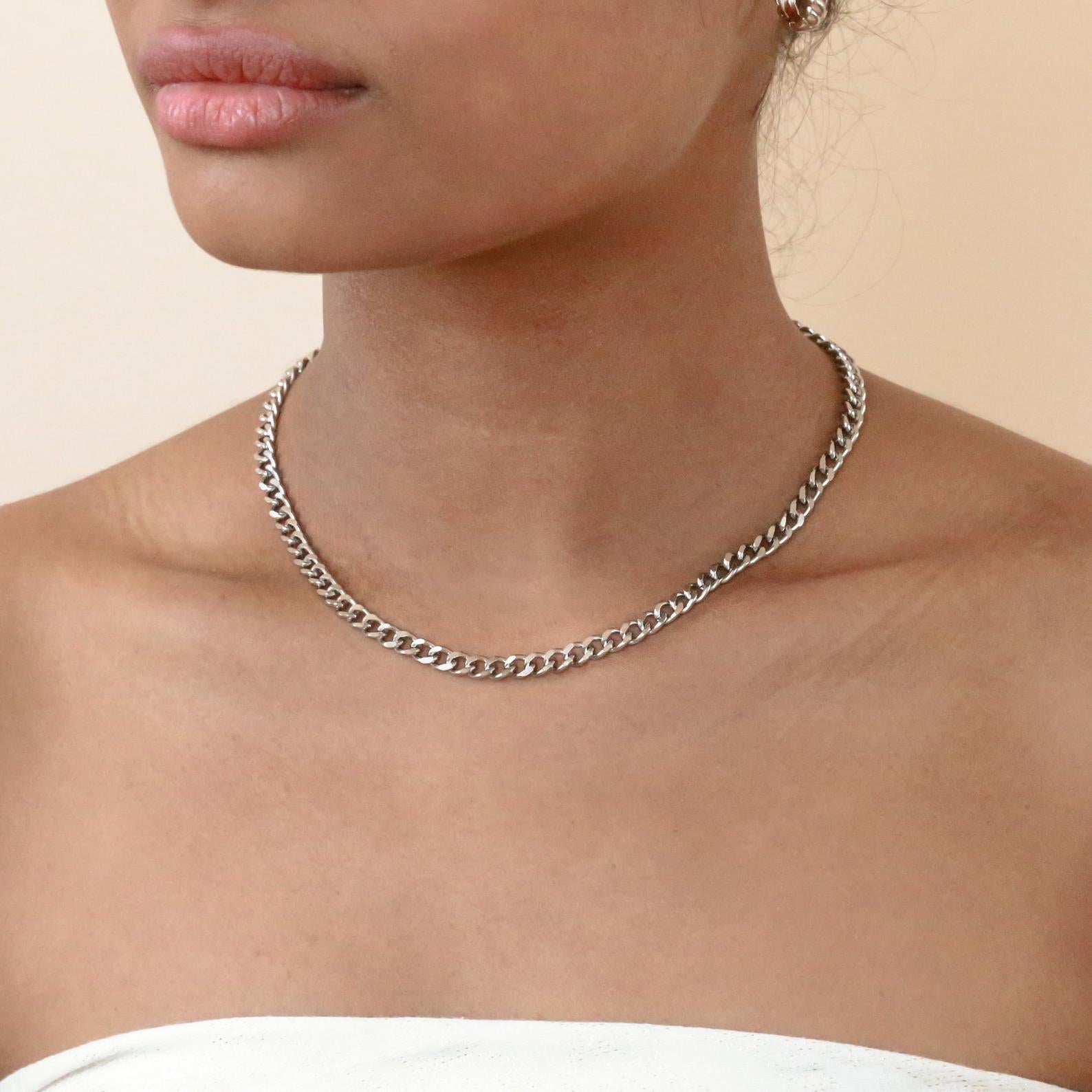 A silver curb chain necklace worn on a model's neck.