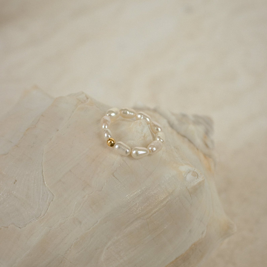 The Pearl Beaded Ring features freshwater pearls and a gold bead, displayed on a large seashell for an effortlessly classy look.
