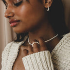 A woman in a cream knit sweater, wearing freshwater pearl earrings, necklace, and the Pearl Beaded Ring, creates a classy accessory ensemble as she gazes downward.