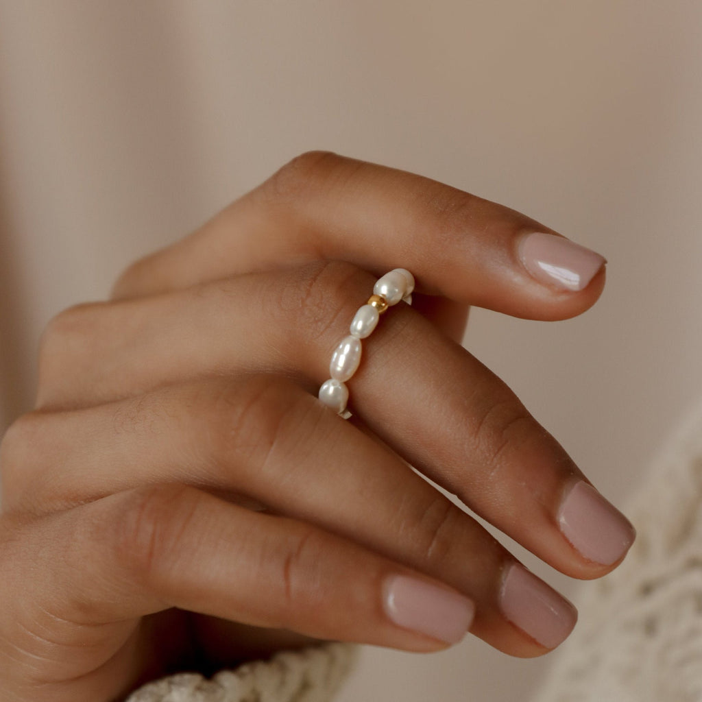 A hand with pale pink nails wears the Pearl Beaded Ring on the index finger, featuring delicate, shimmering freshwater pearls for a classy accessory.