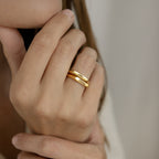 Close-up of a hand wearing two Paris Thin Name Signet Rings with engraved cursive names, stacked together for a chic look and positioned next to the wearer’s face—a perfect stacking ring style.