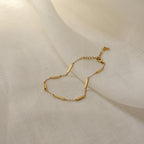 The Abby Bar Link Bracelet is a delicate gold satellite bracelet with small rectangular bar accents, shown on a lightly textured fabric background.